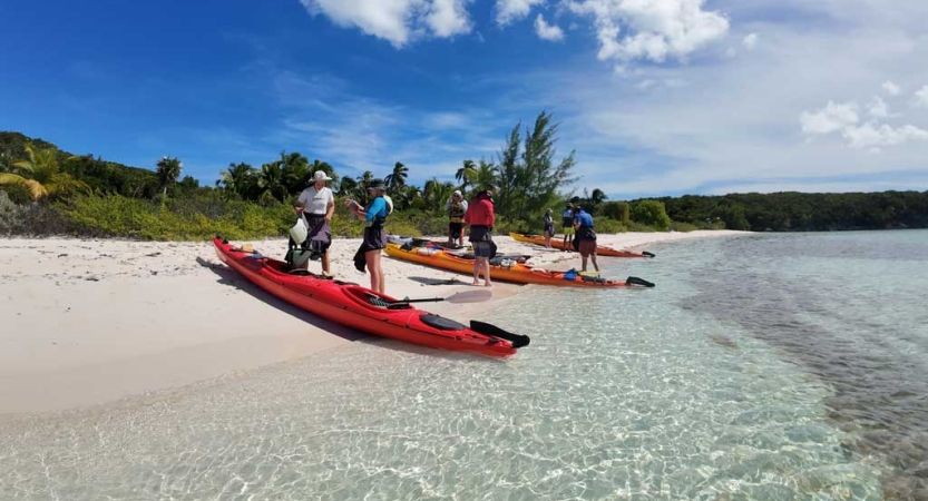 People gather around beached kayaks beside clear water. 